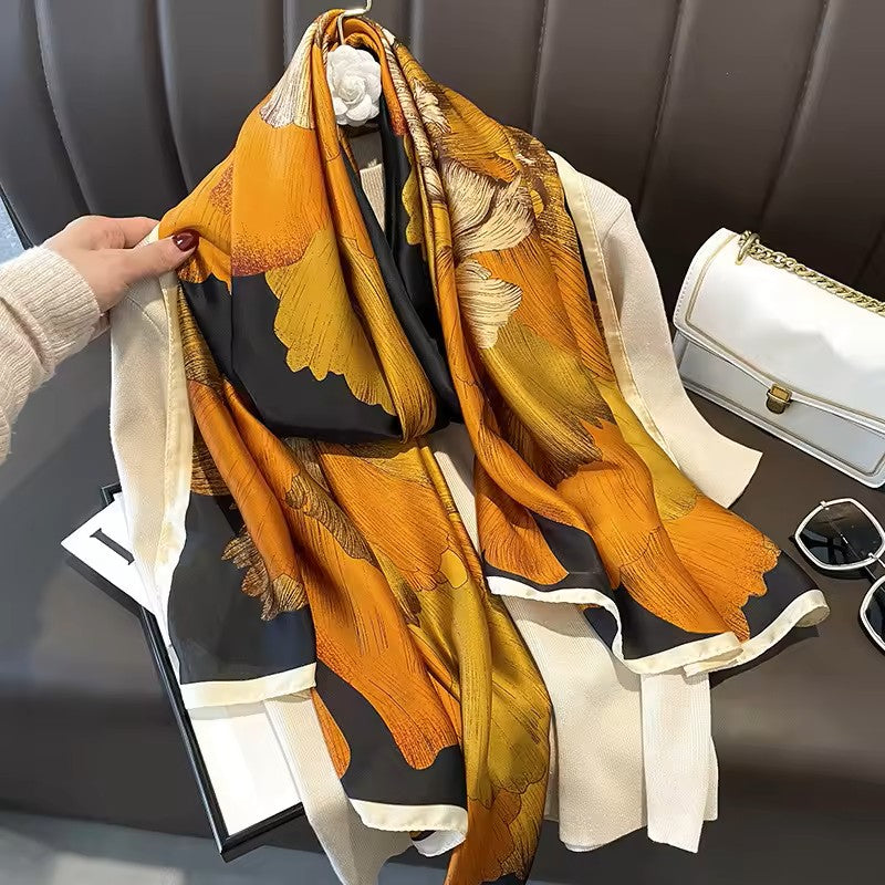 Colorful scarf with floral patterns held by a hand, with a white handbag and sunglasses in the background.
