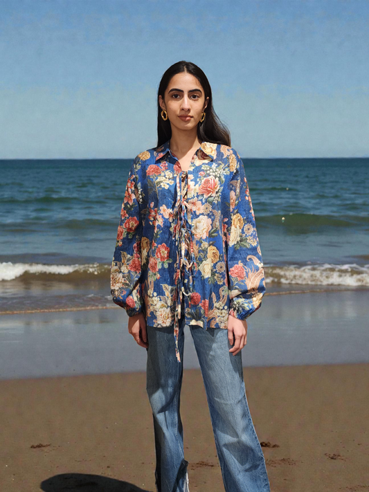Woman standing on a beach wearing a colorful floral shirt and jeans.