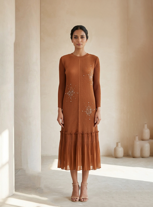 Woman wearing a brown dress with intricate designs in a softly lit room.
