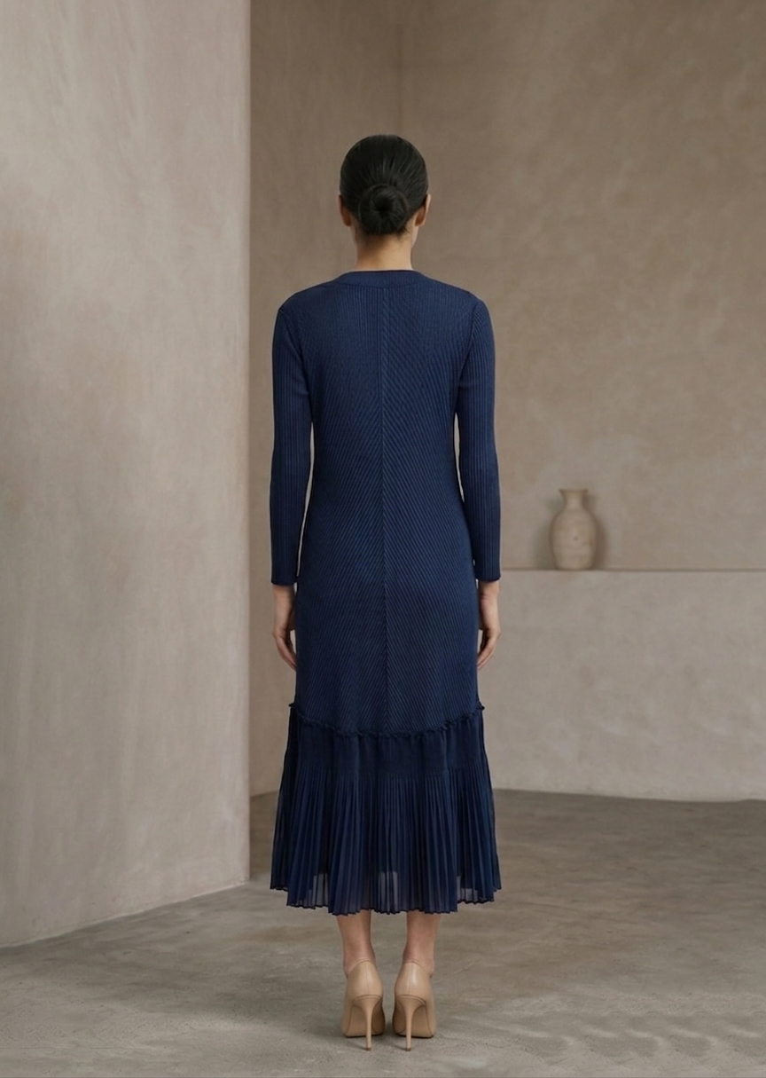 Woman wearing a blue dress standing against a plain wall.