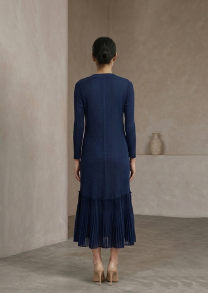 Woman wearing a blue dress standing against a plain wall.