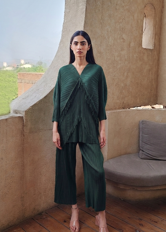 Woman in a green outfit standing on a balcony with a beige wall and wooden floor.