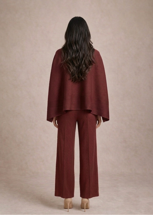 Woman wearing a burgundy outfit with a cape against a beige background