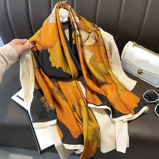 Colorful scarf with floral patterns held by a hand, with a white handbag and sunglasses in the background.