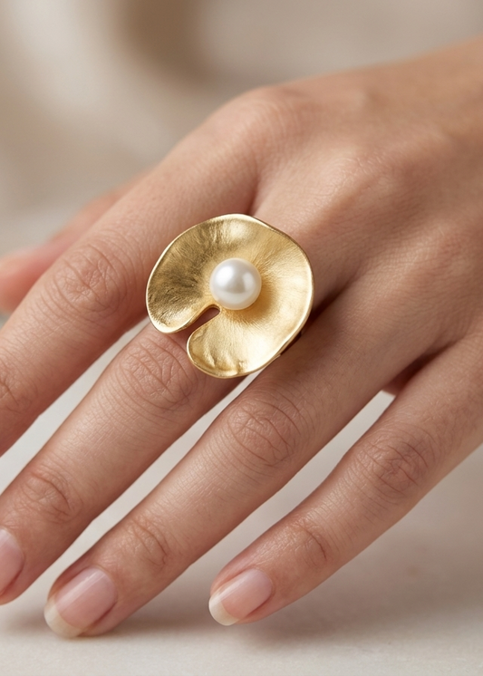 Gold ring with a pearl on a hand against a neutral background