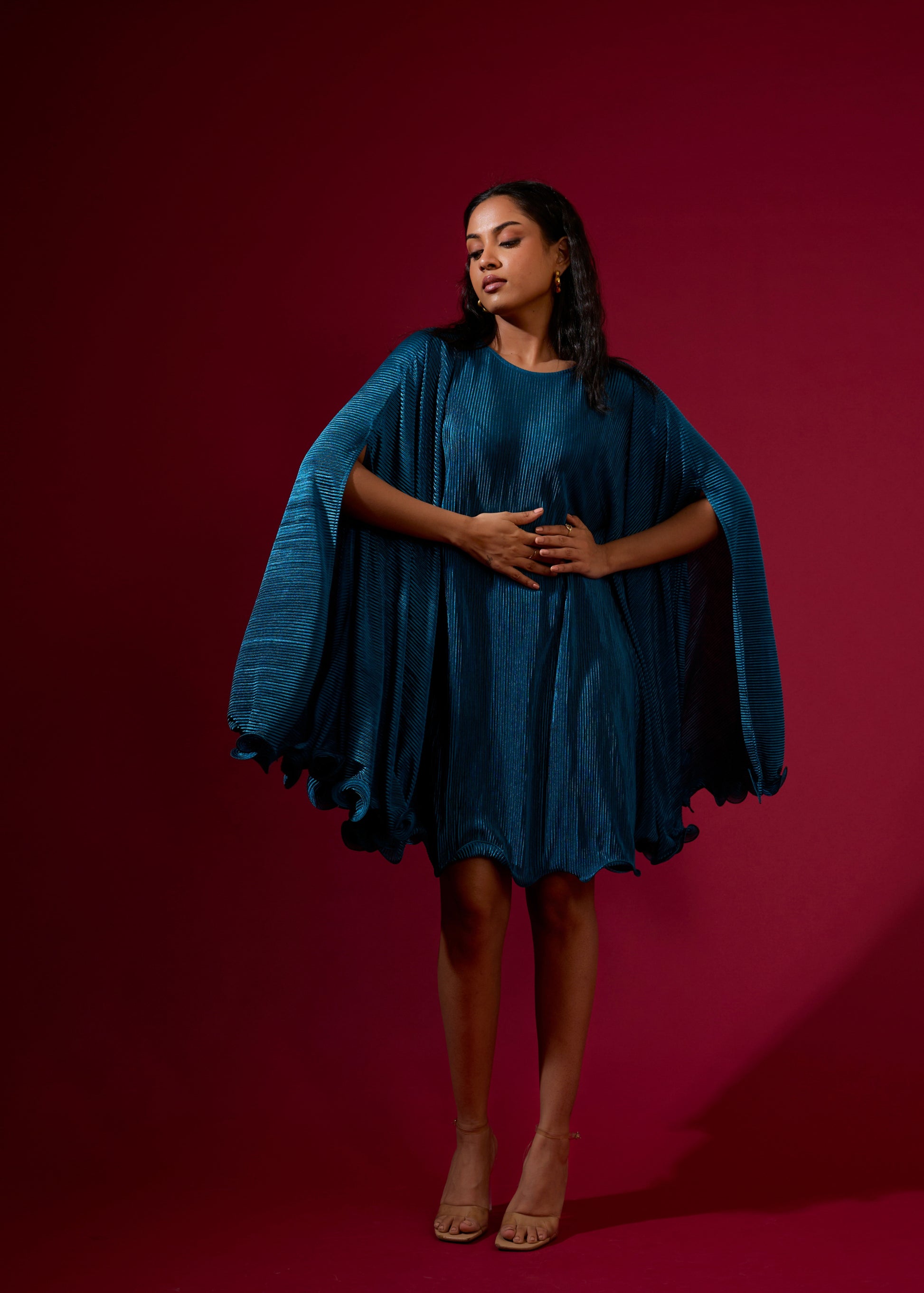 Woman wearing a blue dress with cape sleeves against a red background